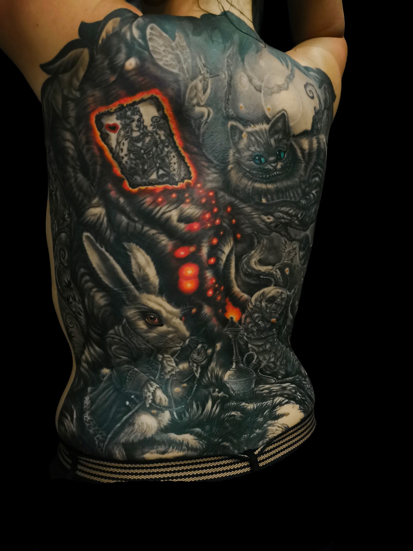 Detailed full back tattoo design of Alice in Wonderland with a rabbit, glowing eyes, and mystical elements