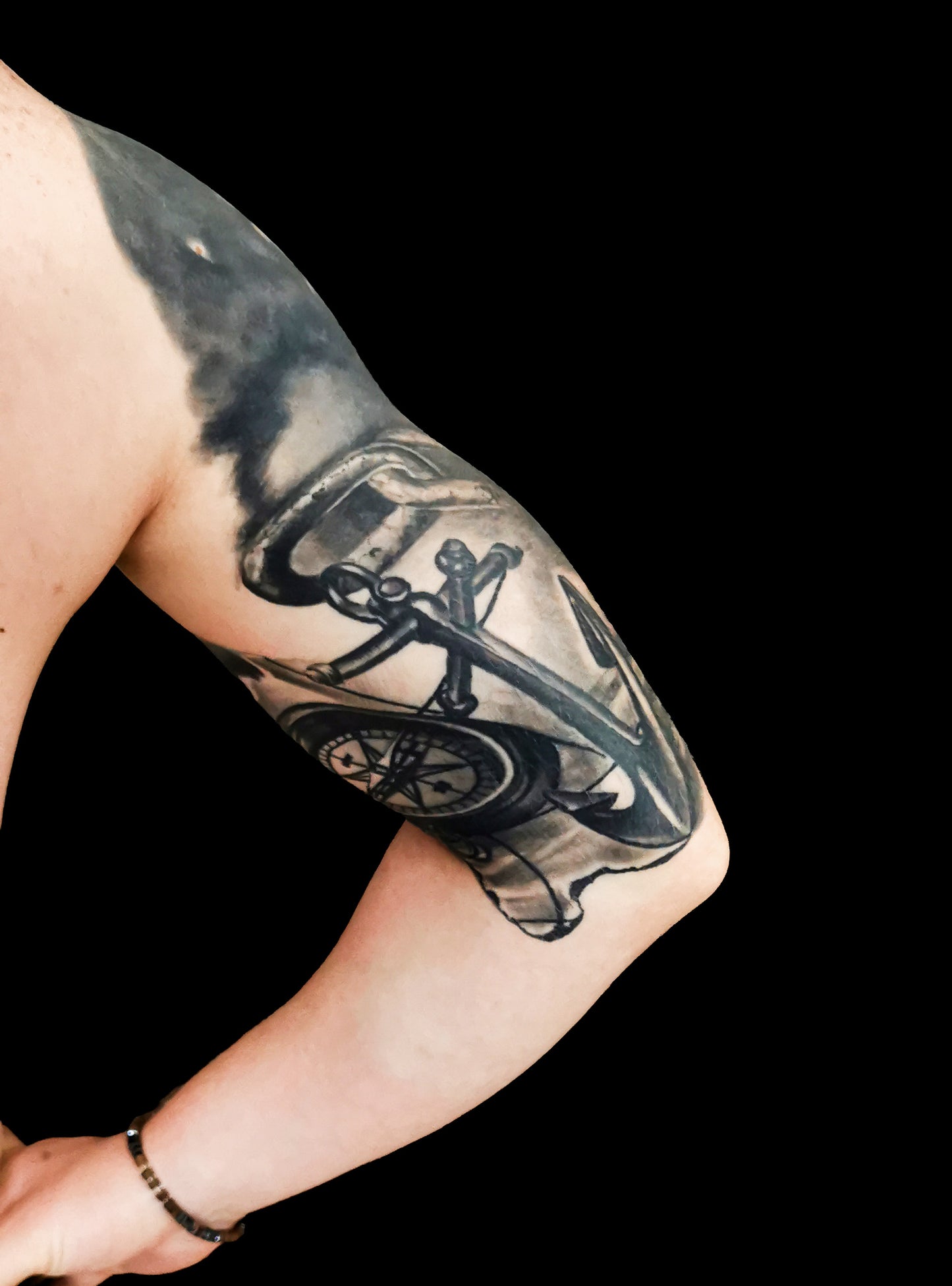 Halfsleeve tattoo on a person's right arm with anchor, compass, map and a ship in storm amongst waves and sunrays from the dark clouds