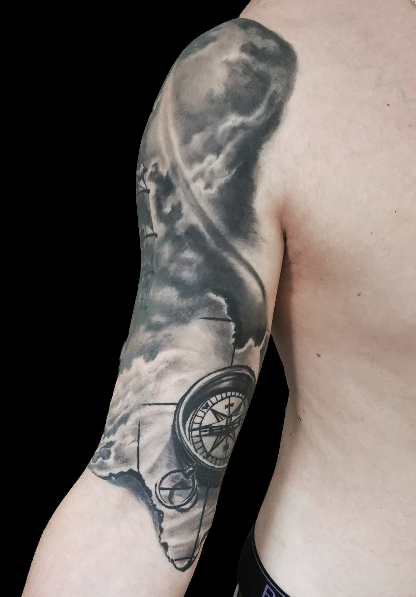 Halfsleeve tattoo on a person's right arm with anchor, compass, map and a ship in storm amongst waves and sunrays from the dark clouds
