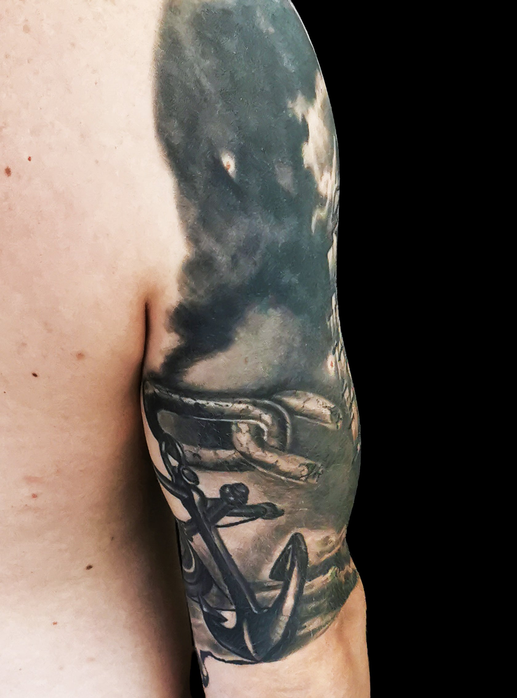 Halfsleeve tattoo on a person's right arm with anchor, compass, map and a ship in storm amongst waves and sunrays from the dark clouds