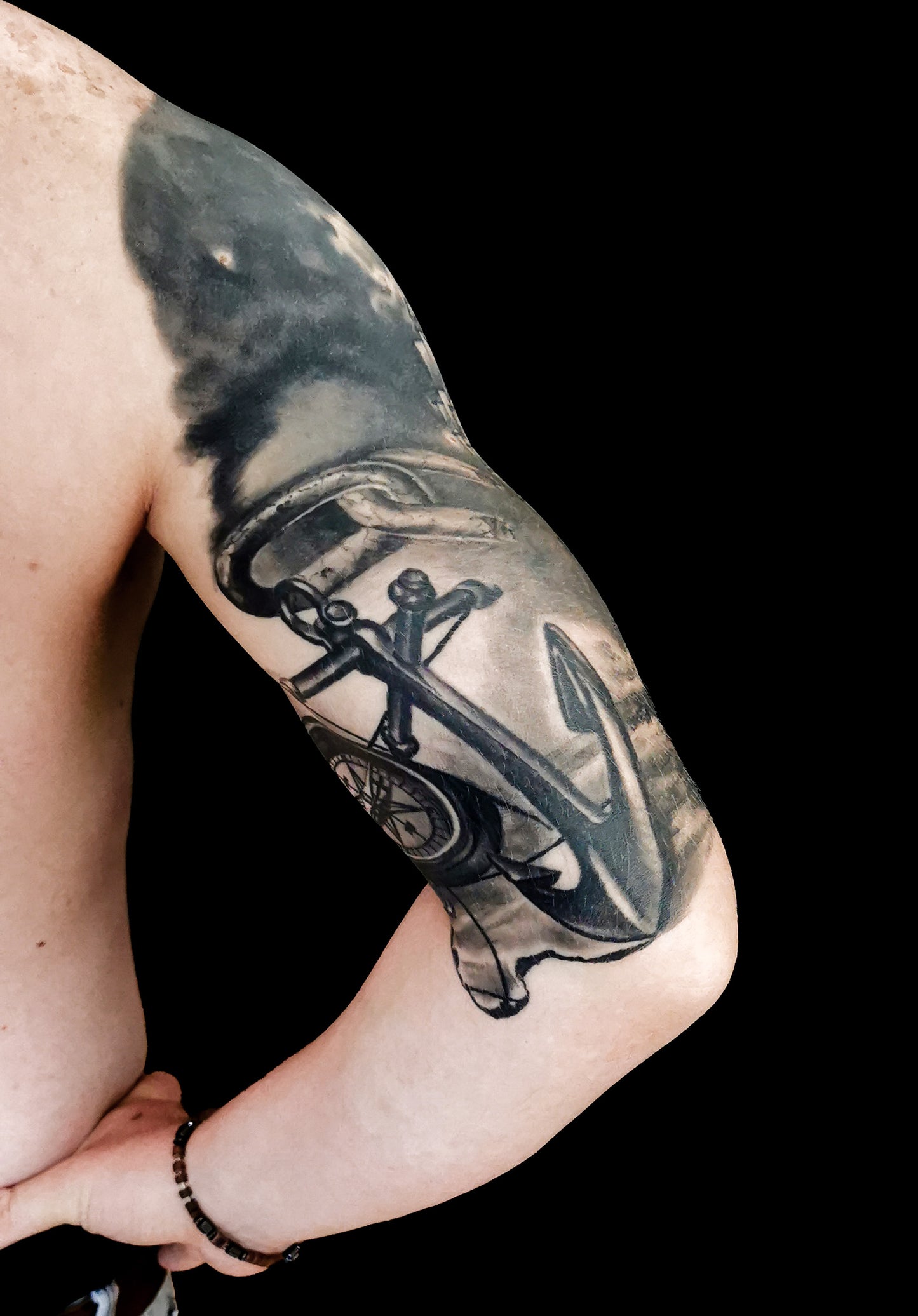 Halfsleeve tattoo on a person's right arm with anchor, compass, map and a ship in storm amongst waves and sunrays from the dark clouds