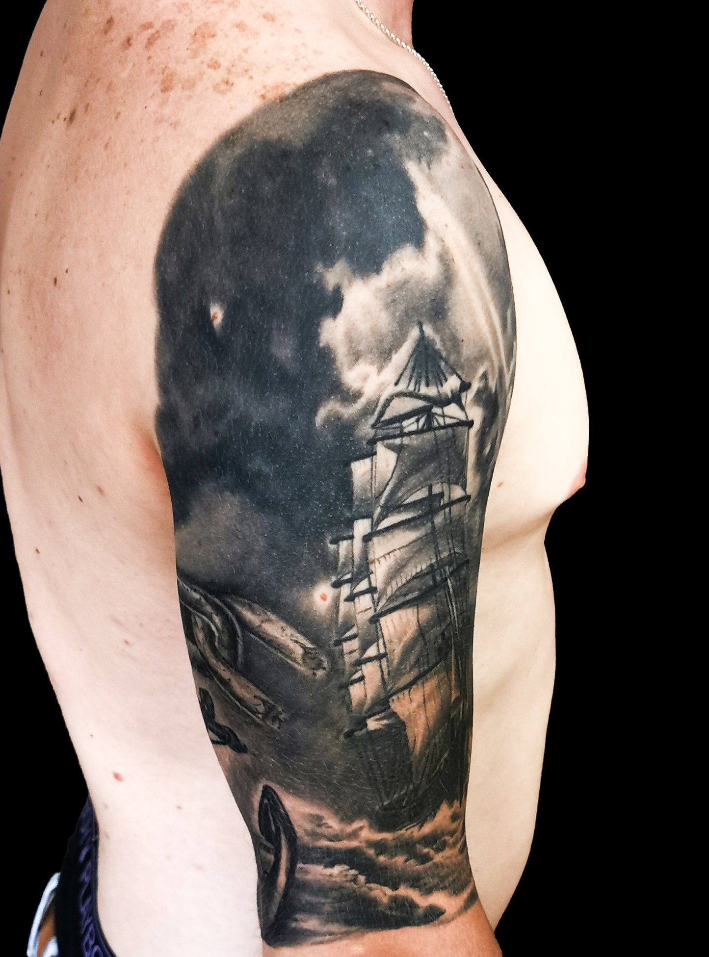 Halfsleeve tattoo on a person's right arm with anchor, compass, map and a ship in storm amongst waves and sunrays from the dark clouds
