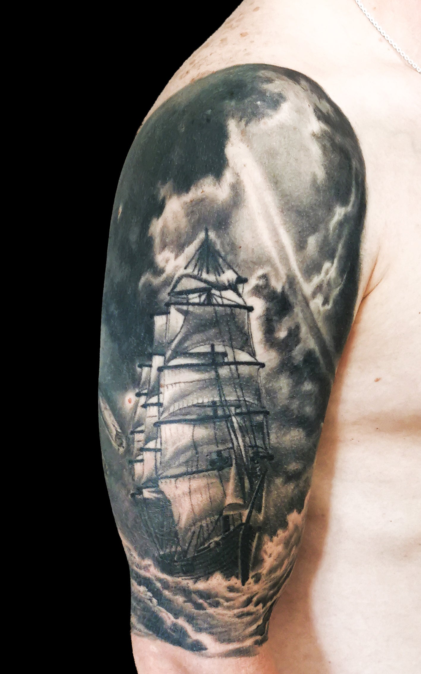 Halfsleeve tattoo on a person's right arm with anchor, compass, map and a ship in storm amongst waves and sunrays from the dark clouds